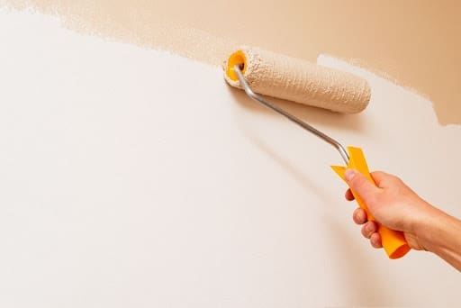 dłoń trzymająca wałek z farbą i malująca ścianę